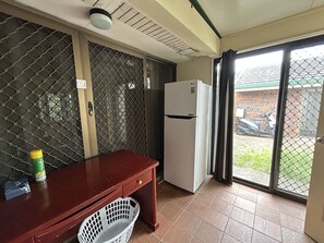 A compact kitchen with a refrigerator, a wooden table, and a window with a view of a parked scooter. - Cozy 1BR Flat in Sunnybank | Solo&Couple Travelers (Sunnybank)