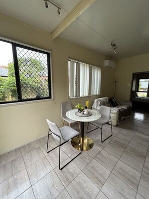 Uma sala de jantar com mesa redonda, duas cadeiras e uma janela com persianas.