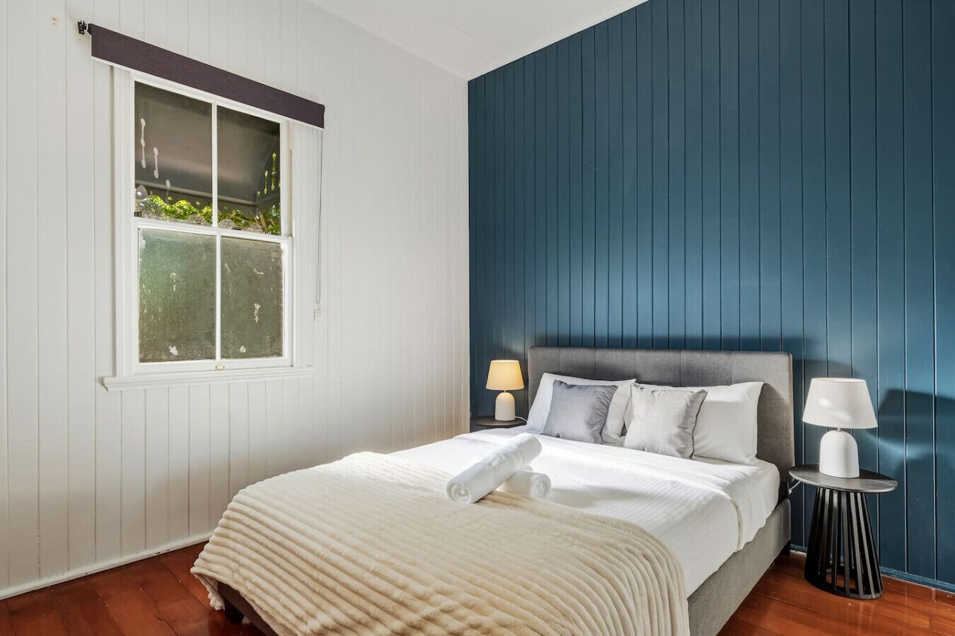 Ein Schlafzimmer mit einem Bett, zwei Nachttischen, einem Fenster und einer blauen Wand.