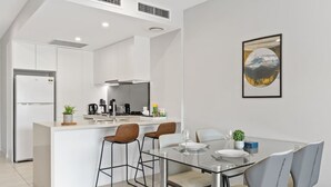 Una cocina moderna con armarios blancos, una isla central con taburetes y una mesa de comedor con sillas.