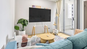 Ein modernes Wohnzimmer mit einem Flachbildfernseher, einer Couch, einem Couchtisch, einem Blumentopf und einer Glastür zum Balkon.
