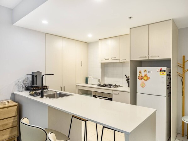 Une cuisine moderne dotée d’un îlot central, de meubles blancs et d’un réfrigérateur encastré.