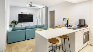 Eine moderne Küche mit einer zentralen Kochinsel, Barhocker, einem Flachbildfernseher und einem Deckenventilator.