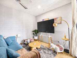 Ein modernes Wohnzimmer mit einem blauen Sofa, einem runden Couchtisch, einem an der Wand befestigten Flachbildfernseher und einer Stehlampe.