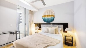 Ein modernes Hotelzimmer mit einem großen Bett, zwei Nachttischlampen, einem Deckenventilator und einem großen Fenster mit Vorhängen.