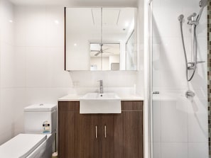 A modern bathroom with a white sink, wooden cabinets, a glass shower enclosure, and a ceiling fan. - Prime CBD Stay | Walk to Queen St Mall | 1 Parking (Brisbane City)