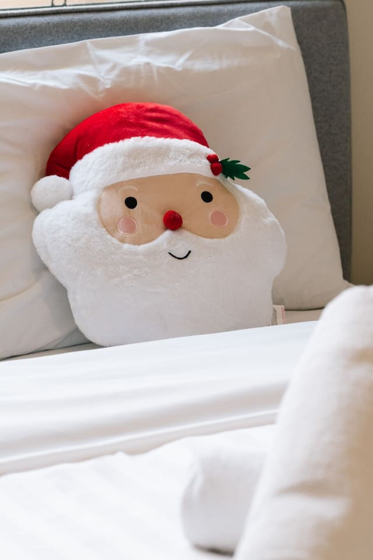 A plush Santa Claus pillow on a bed with white bedding.