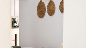 A dining area with a white table, green chairs, and a checkered cushion. There are woven wall decorations and a light fixture above the table. - TRULLO MAMELI - DIEMME STAY (Alberobello)