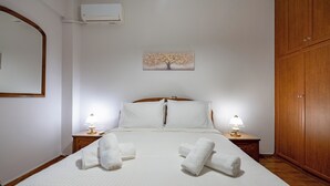 A hotel room with a bed, two bedside tables with lamps, a wooden wardrobe, a painting of a tree, and an air conditioning unit. - Authentic Athens stay in Kypseli by ΜΡS (Athina)