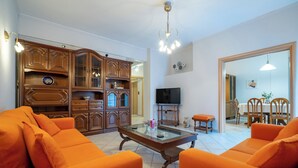 A living room with orange sofas, a glass-top coffee table, wooden cabinets, and a TV. - Authentic Athens stay in Kypseli by ΜΡS (Athina)