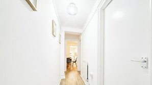 Un corridoio stretto con pareti bianche e pavimento in legno che conduce a una stanza con zona pranzo.