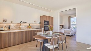 Een moderne keuken met een centraal eiland, een eethoek met een tafel voor vier personen, en een slaapkamer met een bed en uitzicht op de stad.