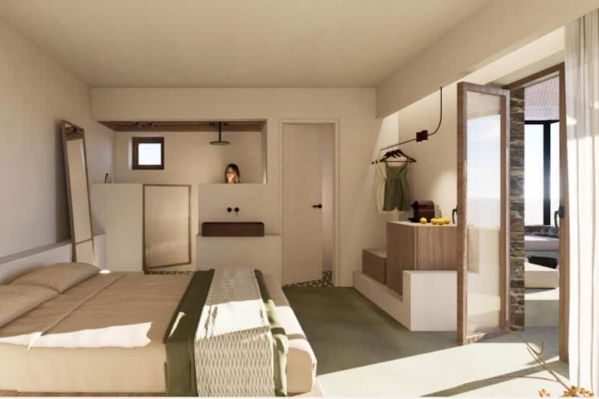 Ein modernes Schlafzimmer mit Bett, einer kleinen Küchenzeile, einem Spiegel und Blick ins Freie.