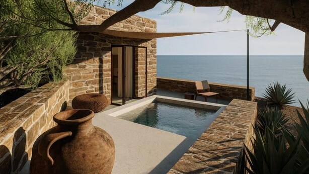 Una piscina infinita de paredes de piedra con vistas al mar, un florero rústico y una zona de estar con mesa y sillas.