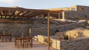 Un espacio al aire libre con patio, paredes de piedra, mobiliario de madera y una estructura de pérgola.