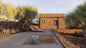 Un edificio moderno de piedra con una ventana pequeña y una puerta, rodeado de vegetación desértica y una piscina cristalina.