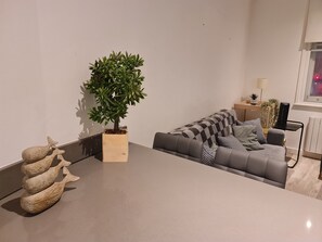Una sala de estar moderna con un sofá gris, una pequeña planta en maceta y una escultura de madera decorativa.