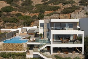 Ein modernes, zweistöckiges Haus mit Swimmingpool, Sitzgelegenheit im Freien und einer Steinmauer.