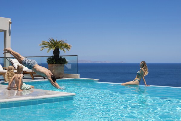 Ein Poolbereich mit Blick auf das Meer, eine Palme und Liegestühle.