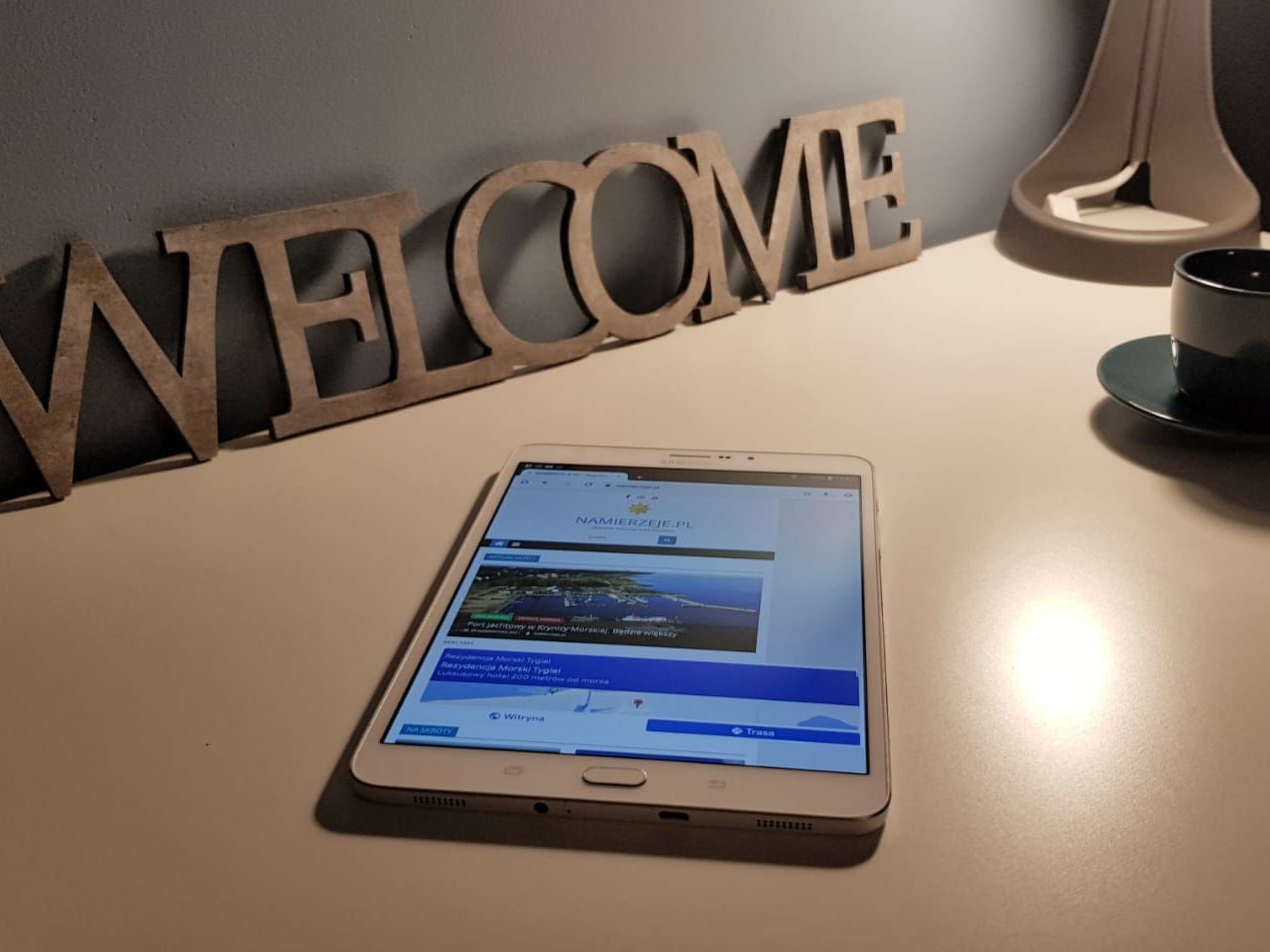 A tablet displaying a website on a table with a 'WELCOME' sign in the background.
