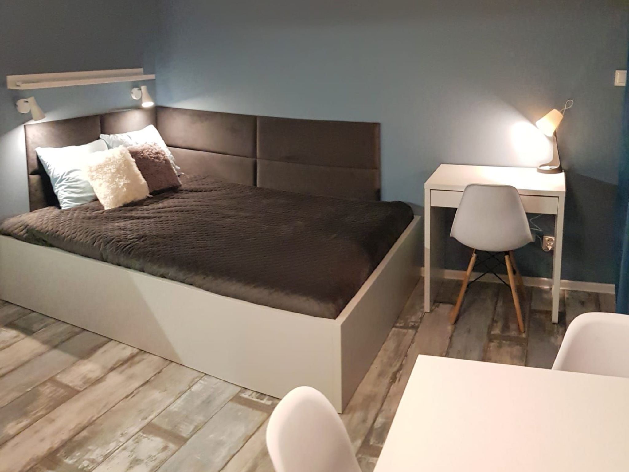 A bedroom with a bed, bedside table, chair, and desk.
