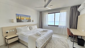 Hotellihuone, jossa on sänky, työpöytä ja taulu, jossa on kuvattuna auringonlasku järven yllä.