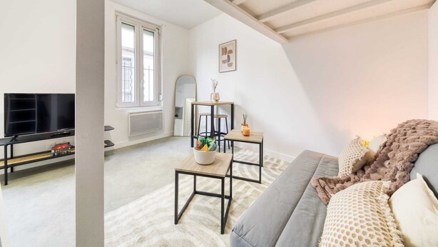 Uma sala de estar moderna com um sofá cinzento, um aparador preto e uma pequena mesa de madeira.