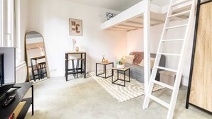 Quarto moderno e bem iluminado, com beliche, escrivaninha com computador, espelho e pequena mesa com objetos decorativos.