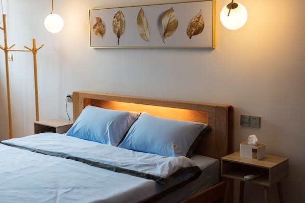 A neatly made bed with blue bedding, a wooden headboard, and a wall-mounted artwork of leaves.