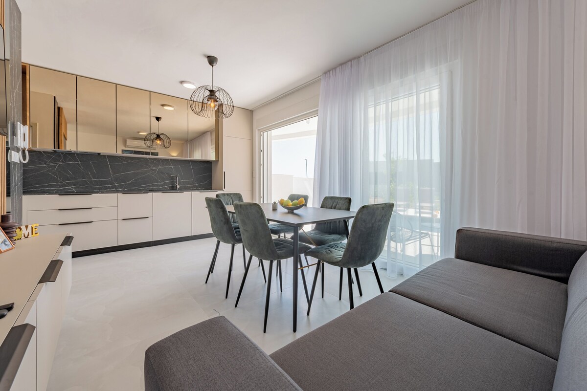 A modern kitchen with a dining area, large windows, and a sofa.