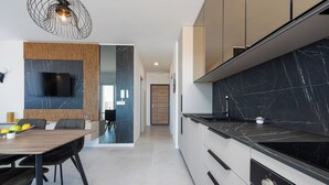 A modern kitchen with a flat-screen TV, a wooden dining table, and a black marble backsplash. - Apartments Twins with private pool  (Novalja)