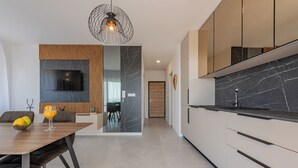 A modern kitchen with a built-in TV, a dining area with a wooden table and chairs, and a kitchen island. - Apartments Twins with private pool  (Novalja)