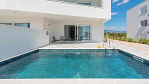 A modern two-story building with a swimming pool, outdoor seating, and a clear view of the mountains. - Apartments Twins with private pool  (Novalja)