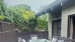 Patio esterno con tavolo in vetro e sedie in metallo, circondato da un molo in legno e una recinzione scura.