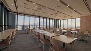 Uma sala de conferências com mesas e cadeiras grandes, piso coberto por carpete e vista para as montanhas através de amplas janelas.