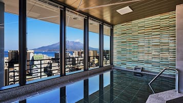 A modern indoor pool with large windows offering a view of a cityscape and mountains.