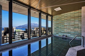 Ein moderner, überdachter Pool mit großen Fenstern und Blick auf eine Stadtlandschaft und Berge.