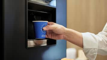 A hand holding a blue disposable cup at a coffee machine.