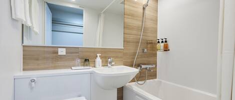 A modern bathroom with a sink, mirror, shower, and toiletries.