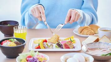 A person dining with a variety of dishes including a salad, bread, and a croissant.