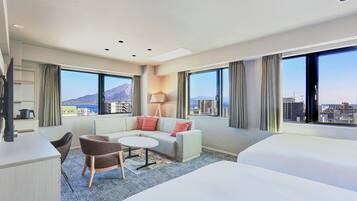 A hotel room with a bed, a sofa, a small table, and a chair. There are large windows with curtains and a view of buildings.