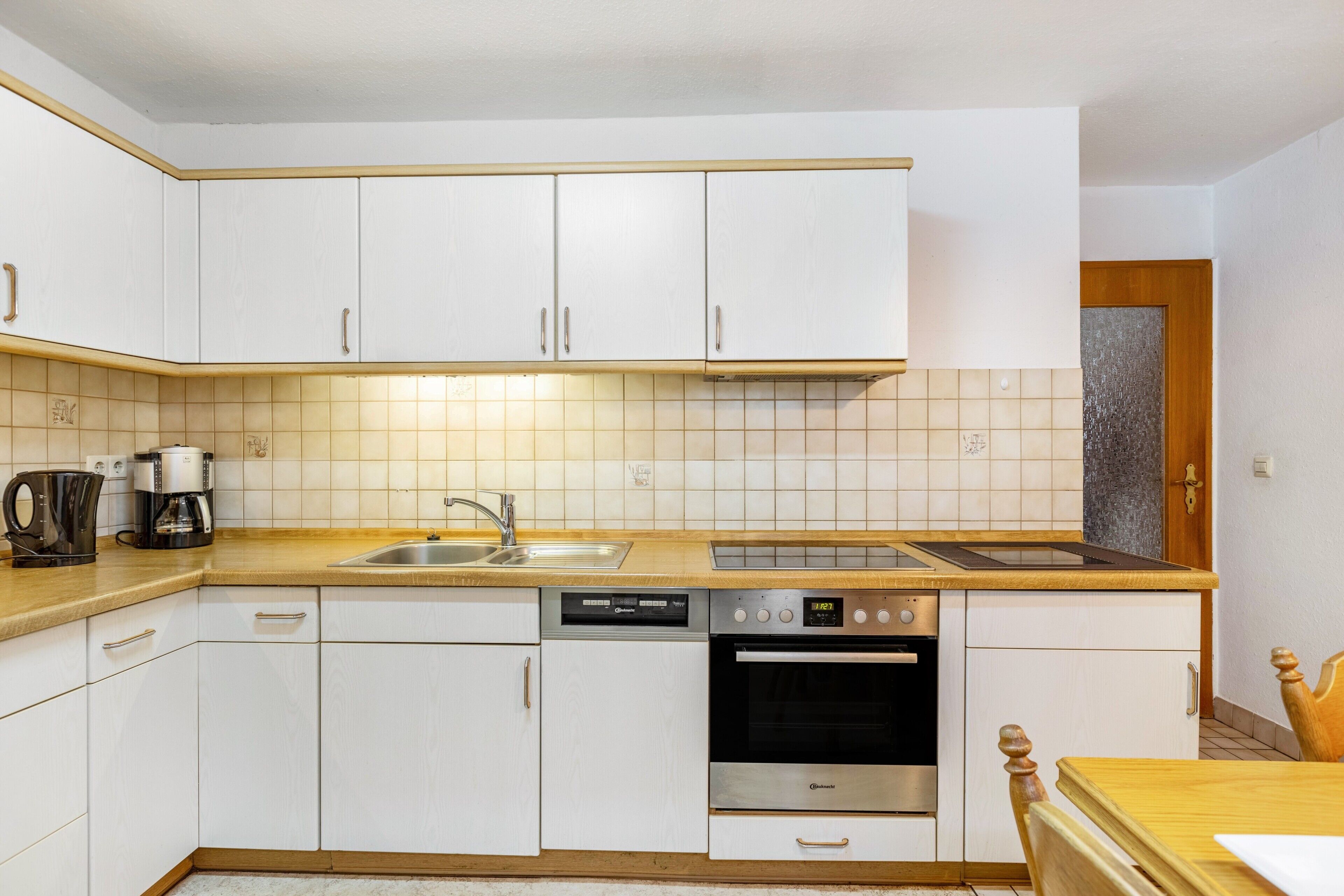 A compact kitchen with white cabinets, a dishwasher, an oven, a coffee maker, and a wooden countertop.