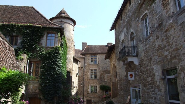Una calle estrecha con edificios de piedra, una torre y un letrero que indica un hotel.