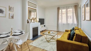 Un salon moderne avec une cheminée, un canapé, une table à manger pour quatre personnes et un téléviseur.