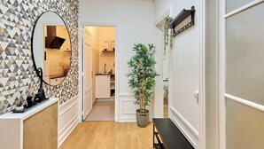 Un couloir avec un mur orné d’un motif géométrique, un miroir, une plante en pot et un banc.