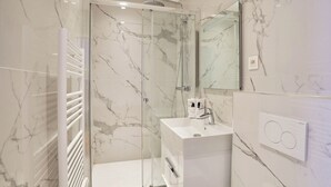 Ein modernes Badezimmer mit einer gläsernen Duschkabine, einem weißen Waschbecken und einer Wand mit Marmorplatten.