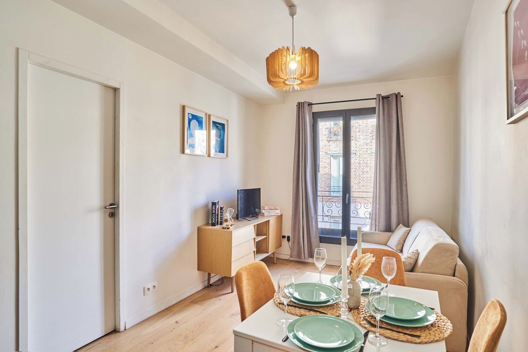 A compact living space with a dining area, a sofa, a TV on a wooden cabinet, and a window with curtains.