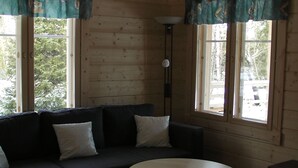 Una habitación acogedora con un sofá de seccional color oscuro, una pequeña mesa redonda y amplias ventanas con cortinas.