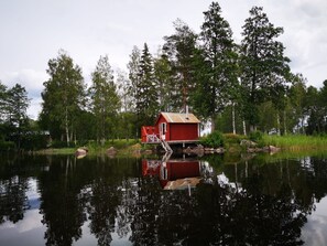 A small red cabin on stilts by a calm lake, surrounded by dense trees. - in Hagfors mit Großem Garten by Interhome (Kyrkheden)