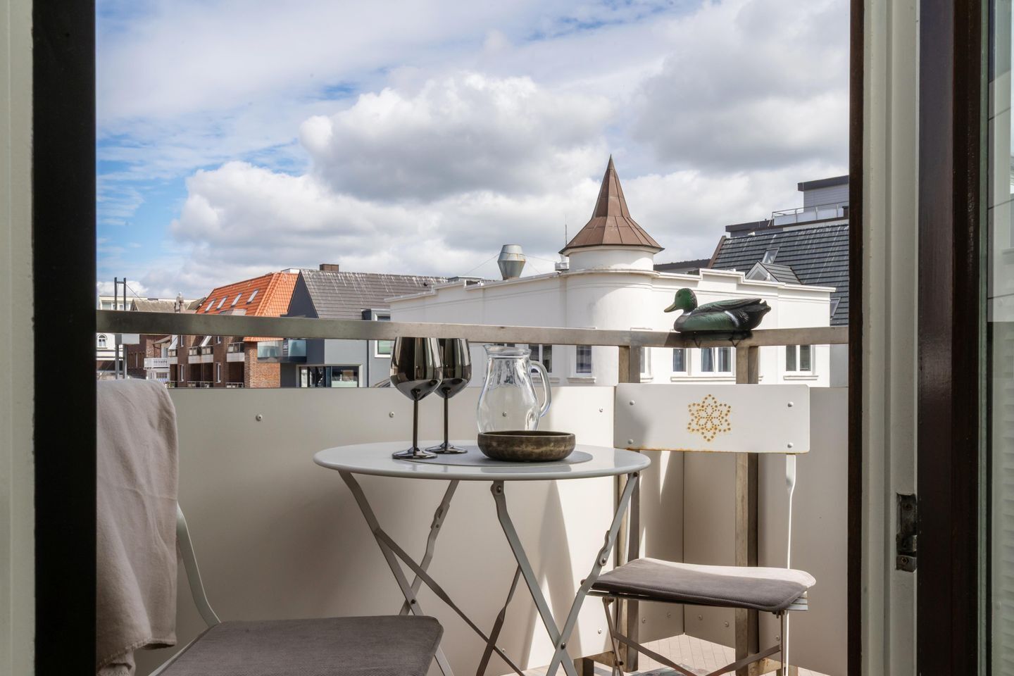 A balcony with a table, two wine glasses, a bowl, and a duck statue.